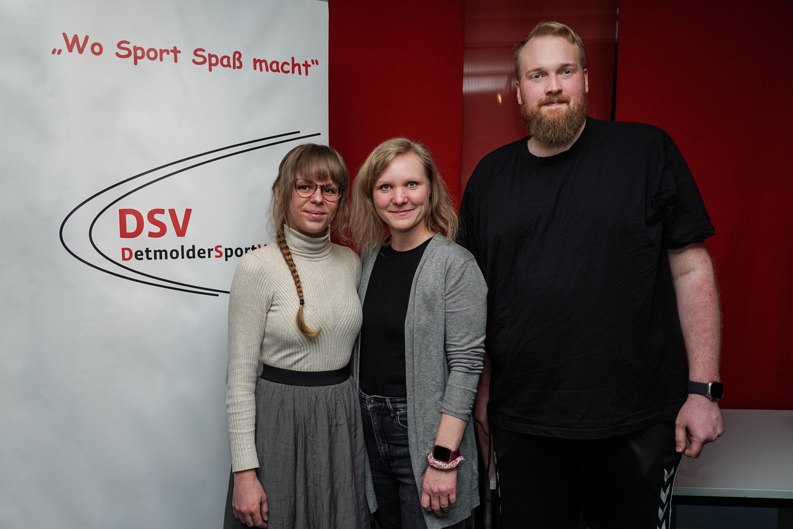 Drei Personen stehen vor einem Banner. Auf dem Banner steht "Wo Sport Spaß macht" und "DSV DetmolderSport".